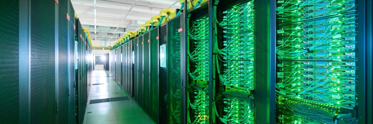 Der Supercomputer SuperMUC-NG am Leibniz-Rechenzentrum: Mehrere Serverschränke bilden einen engen Gang, zahlreiche grüne LEDs blinken.