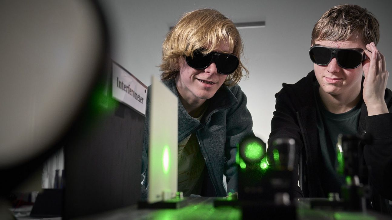 Two boys wearing protective goggles infront of an optical experiment with green lasers. 